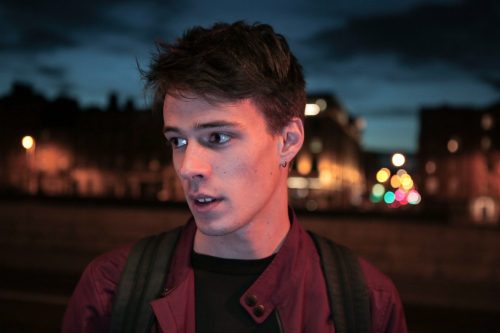 A young man stands at night on a well lit street