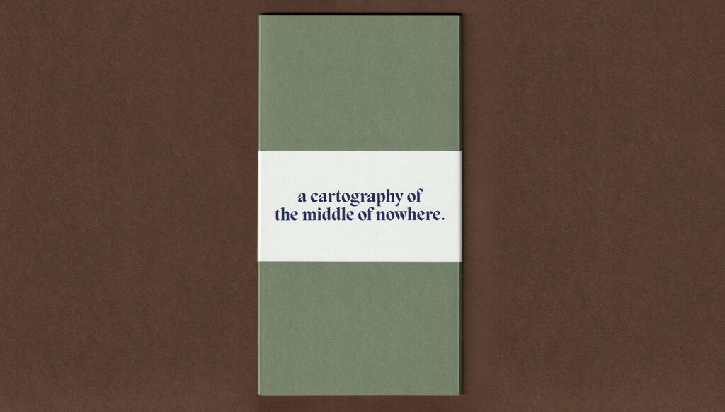 An image of a rectangular green map placed against a rich brown background. The map is bound by a cream slip wrapped around the centre. The slip states the title of the map in indigo Migra font: a cartography of the middle of nowhere