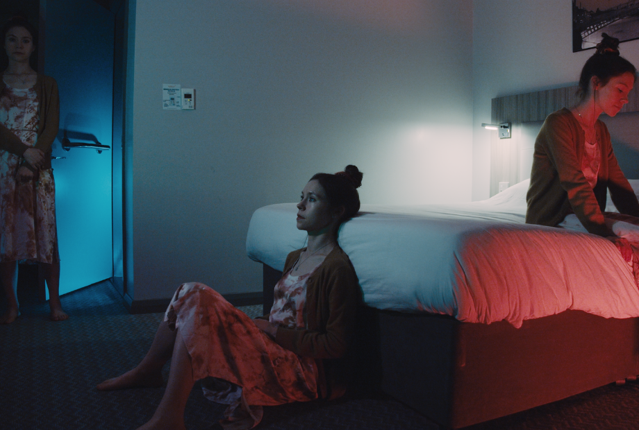 A woman sits on the floor of a hotel room looking at a TV screen.
