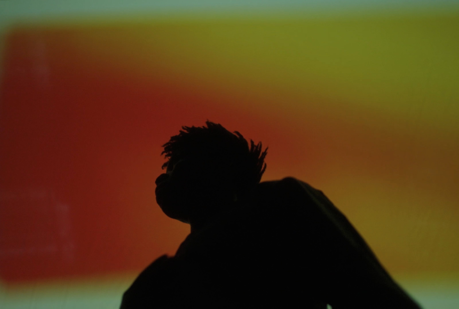 A shadowed figure in relief against an orange and yellow background.