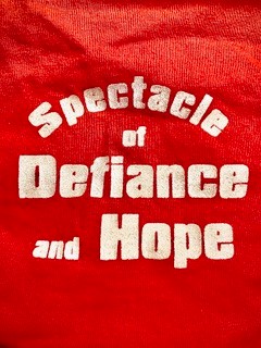A red piece of fabric with the white text "Spectacle of Defiance and Hope" on it