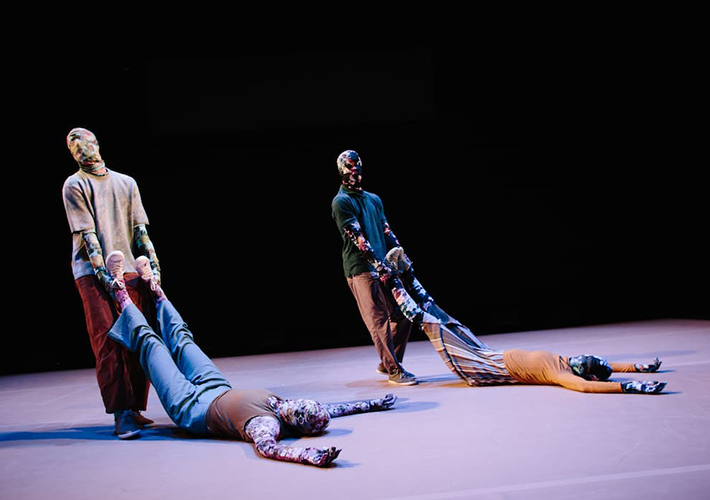There are four dancers all wearing full-body floral morph suits. Two dancers are positioned on the floor, while the other two dancers are being dragged by the two standing dancers. We see that are on the floor are being positioned into an L shape by the dancers that are standing.