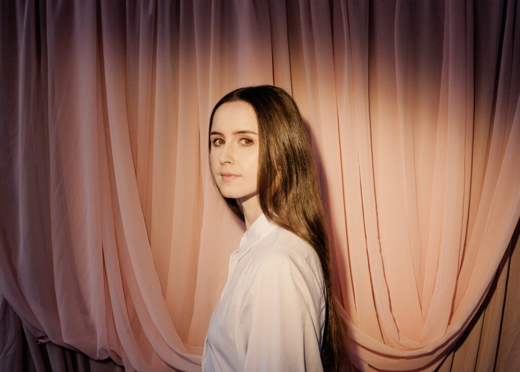 Rachael Lavelle looking over their left shoulder in front of a curtain