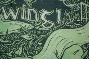 A close-up of an artwork detail on the Project billboard. Text reads “-wing! (Hooray)" against a green and black drawing of water overflowing and dense foliage.