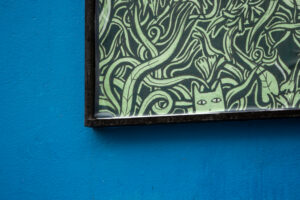 A close-up of an artwork detail on the Project billboard. The artwork shows a green and black drawing of a cat peering out over the bottom frame of the billboard, against a backdrop of dense foliage.