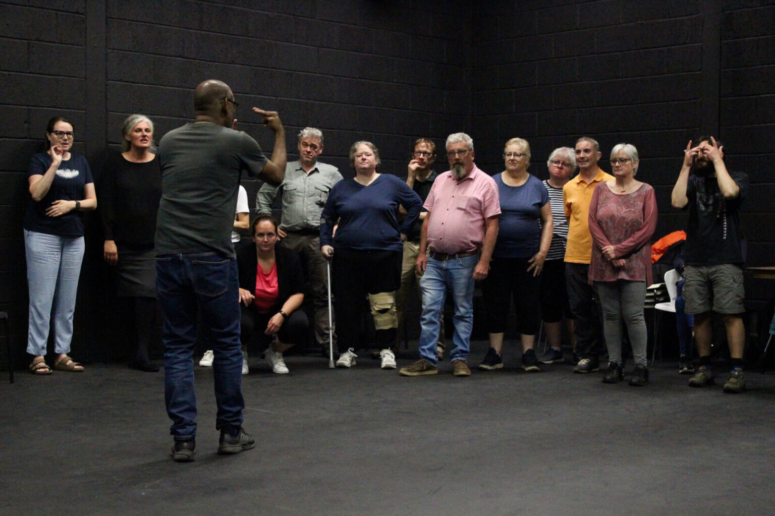 A group of people looking at a performer in a black box studio room