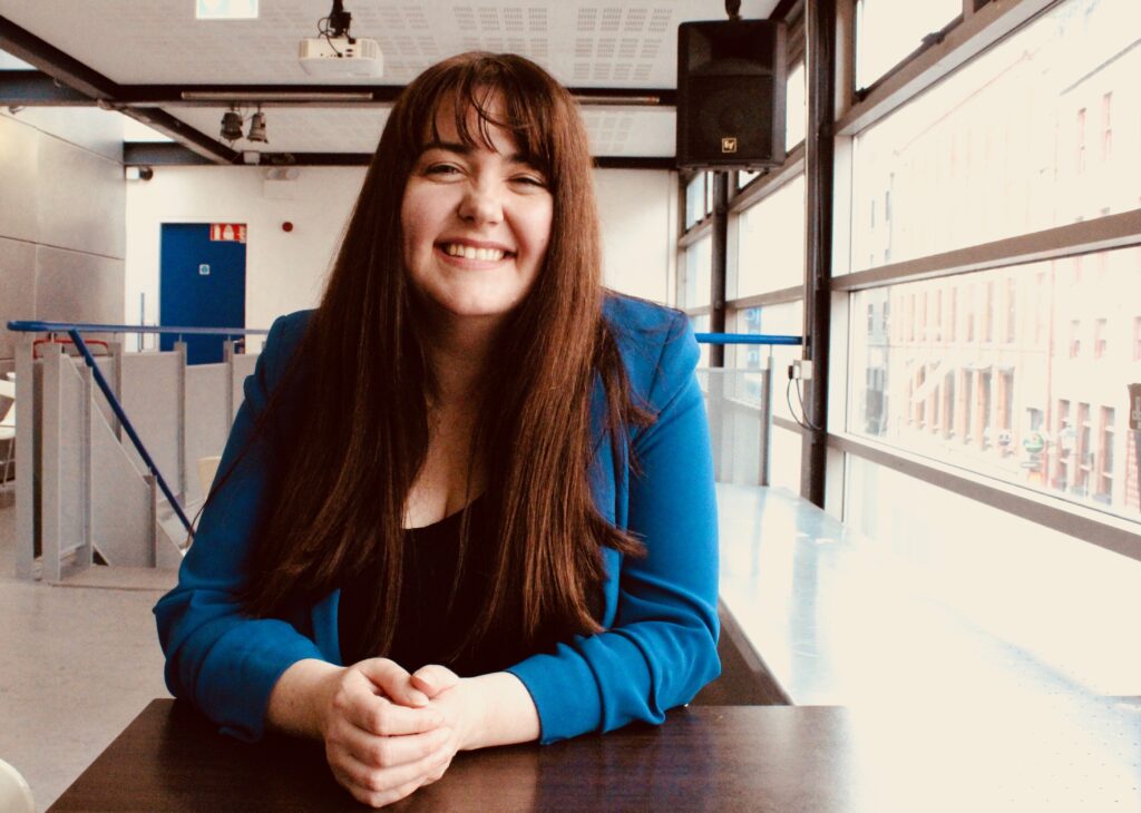 A woman in a blue jacket sits at a table smiling