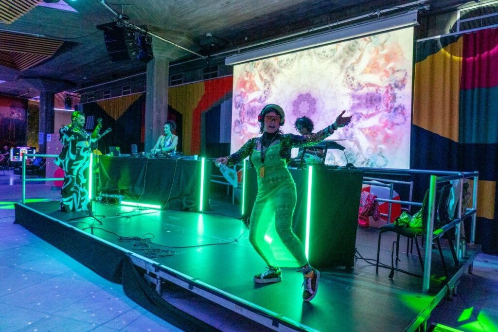DJs and dancers are flooded with bright colour lighting.